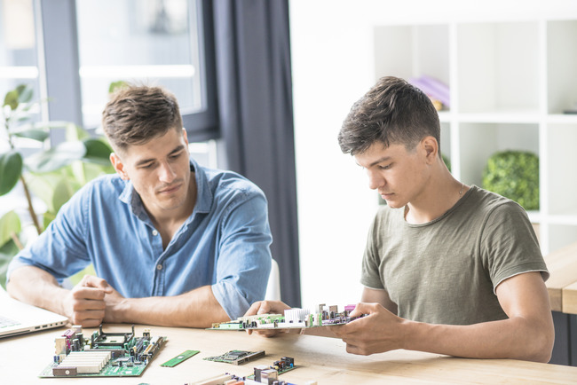 Two young men focused on electronics, working diligently at a table with various tools and components.